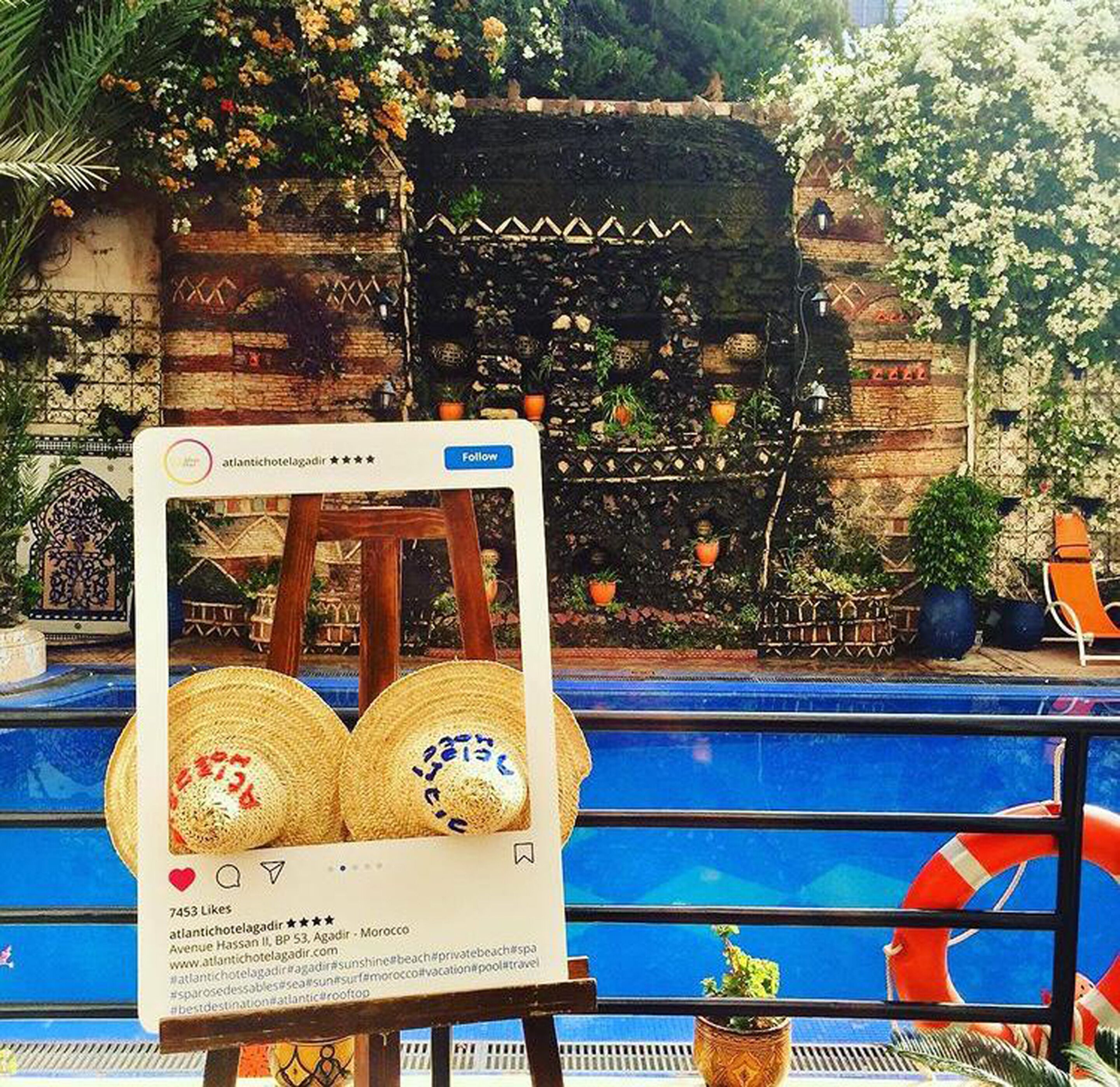 A pool area with a wooden deck, a signboard, and a decorative wall with plants and flowers.