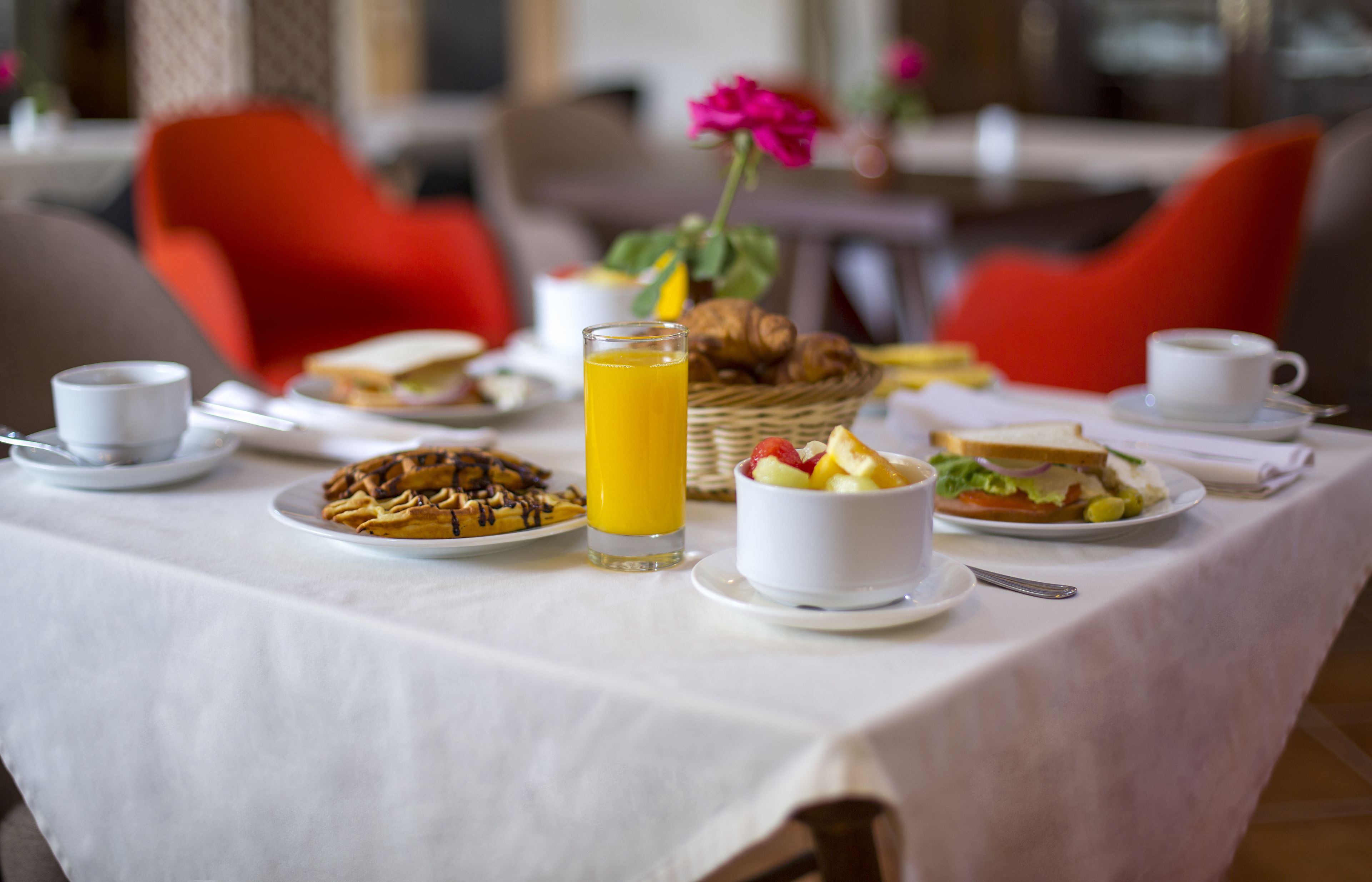 A breakfast table set with various dishes, including waffles, a glass of orange juice, and a bowl of fruit salad.