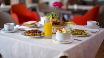 A breakfast table set with various dishes, including waffles, a glass of orange juice, and a bowl of fruit salad.