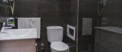 Un baño moderno con lavamanos blanco, inodoro y cabina de ducha con mampara de vidrio.