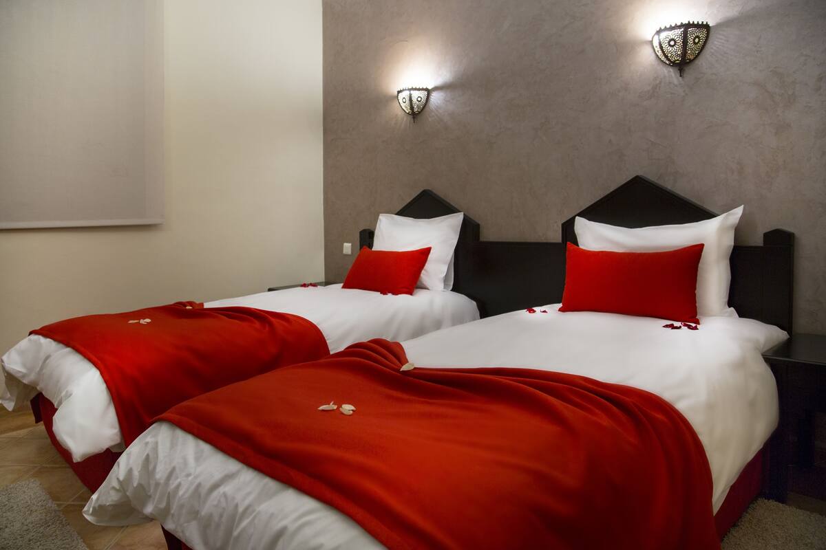 Two beds with red and white bedding, a grey wall, and two wall-mounted light fixtures.