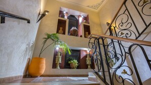 A staircase with ornate metal railings, a potted plant, and a view of a room with a window and decorative items. - Atlantic Hotel Agadir (Agadir)