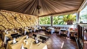 A restaurant with multiple tables set for dining, a stone wall, and large windows with a view of greenery. - Atlantic Hotel Agadir (Agadir)