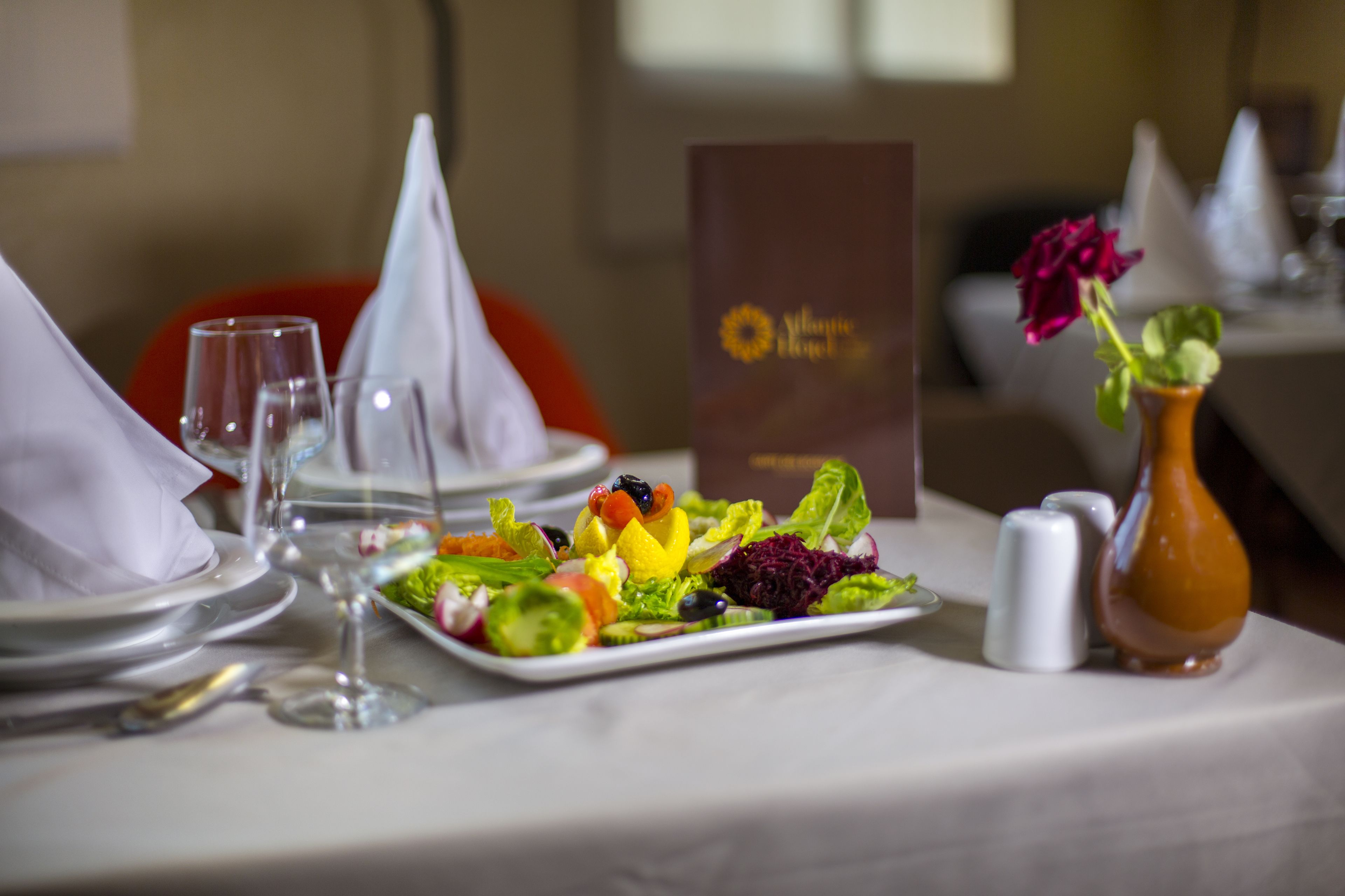 A dining table set with plates, glasses, a salad, and a vase with a rose.