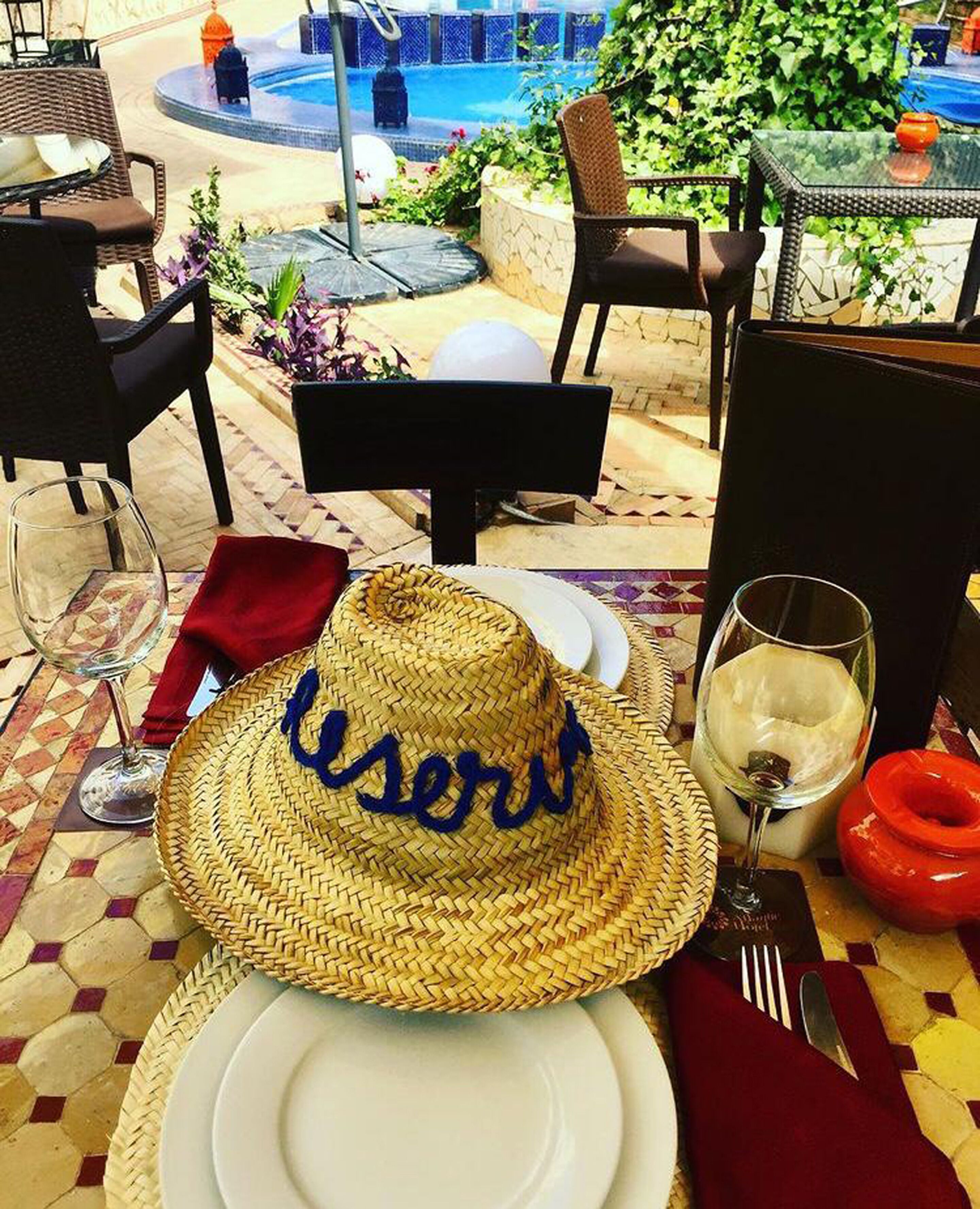Un coin repas avec une table dressée pour deux personnes, comprenant un chapeau de paille orné du mot «utilisateur» brodé, un verre à vin et une assiette.