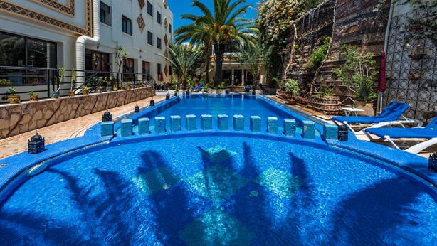 A large, clear swimming pool with blue tiles, surrounded by lounge chairs and palm trees. - Atlantic Hotel Agadir (Agadir)
