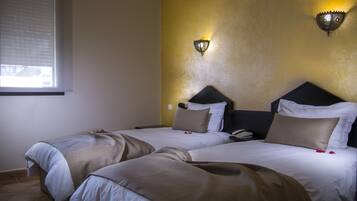 A hotel room with two beds, a bedside table with a phone, and a wall-mounted light fixture.
