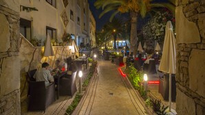 An outdoor dining area with tables and chairs, palm trees, and a pathway. - Atlantic Hotel Agadir (Agadir)