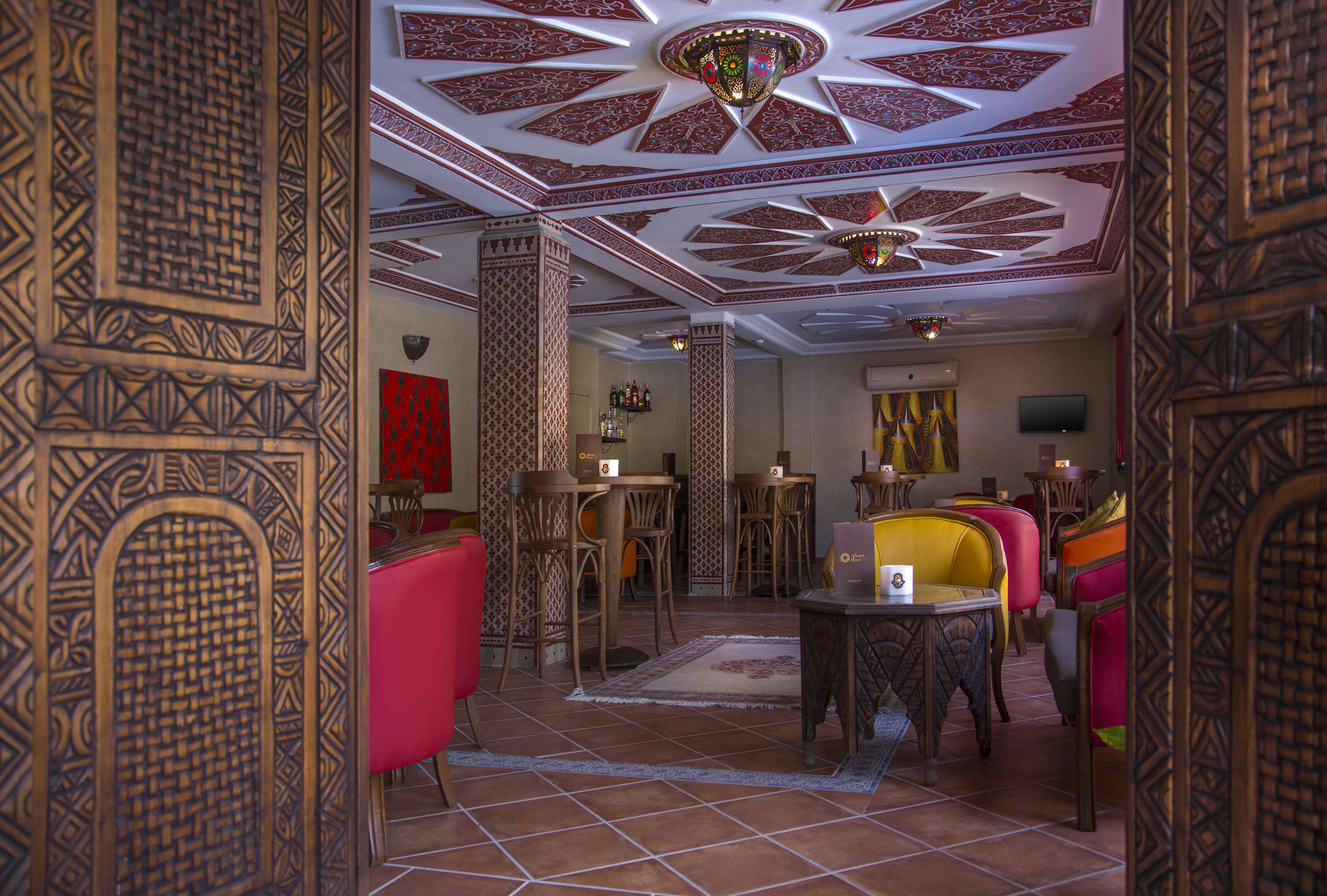 Un interior tradicional con elaboradas esculturas de madera, una pared roja y diversas opciones de asientos, incluyendo una mesa con una silla amarilla.