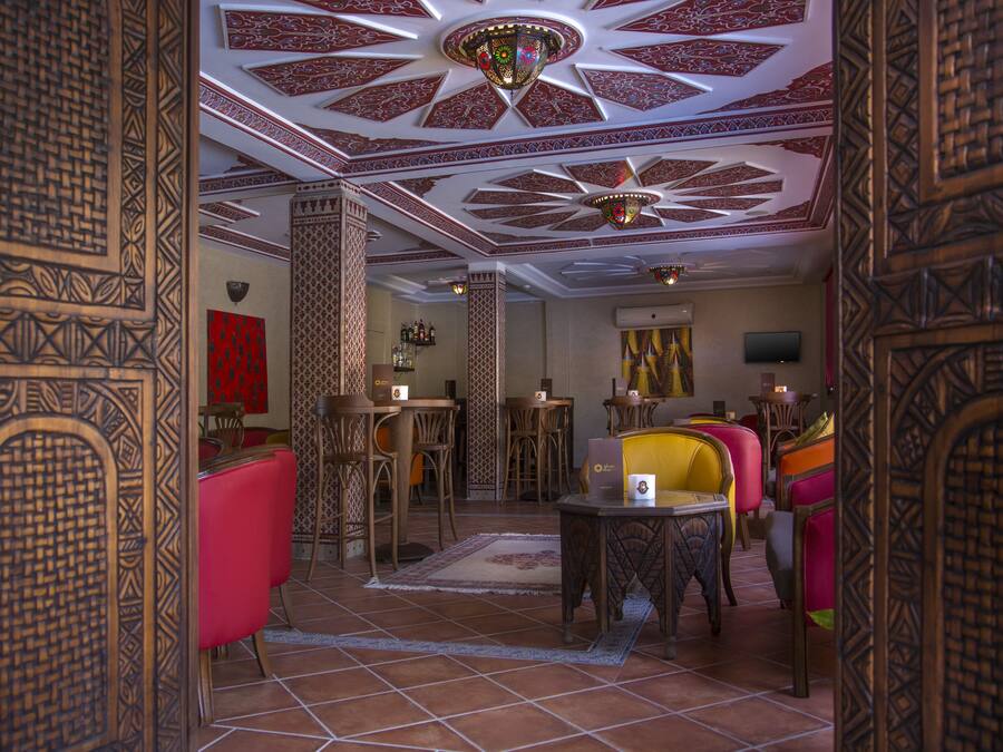 Un interior tradicional con elaboradas esculturas de madera, una pared roja y diversas opciones de asientos, incluyendo una mesa con una silla amarilla.
