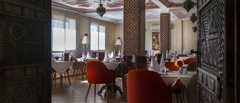 A dining area with red chairs, white tables, and patterned columns.