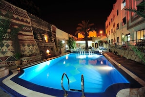 A swimming pool with a stone wall and palm trees, surrounded by a building with a patterned facade. - Atlantic Hotel Agadir (Agadir)