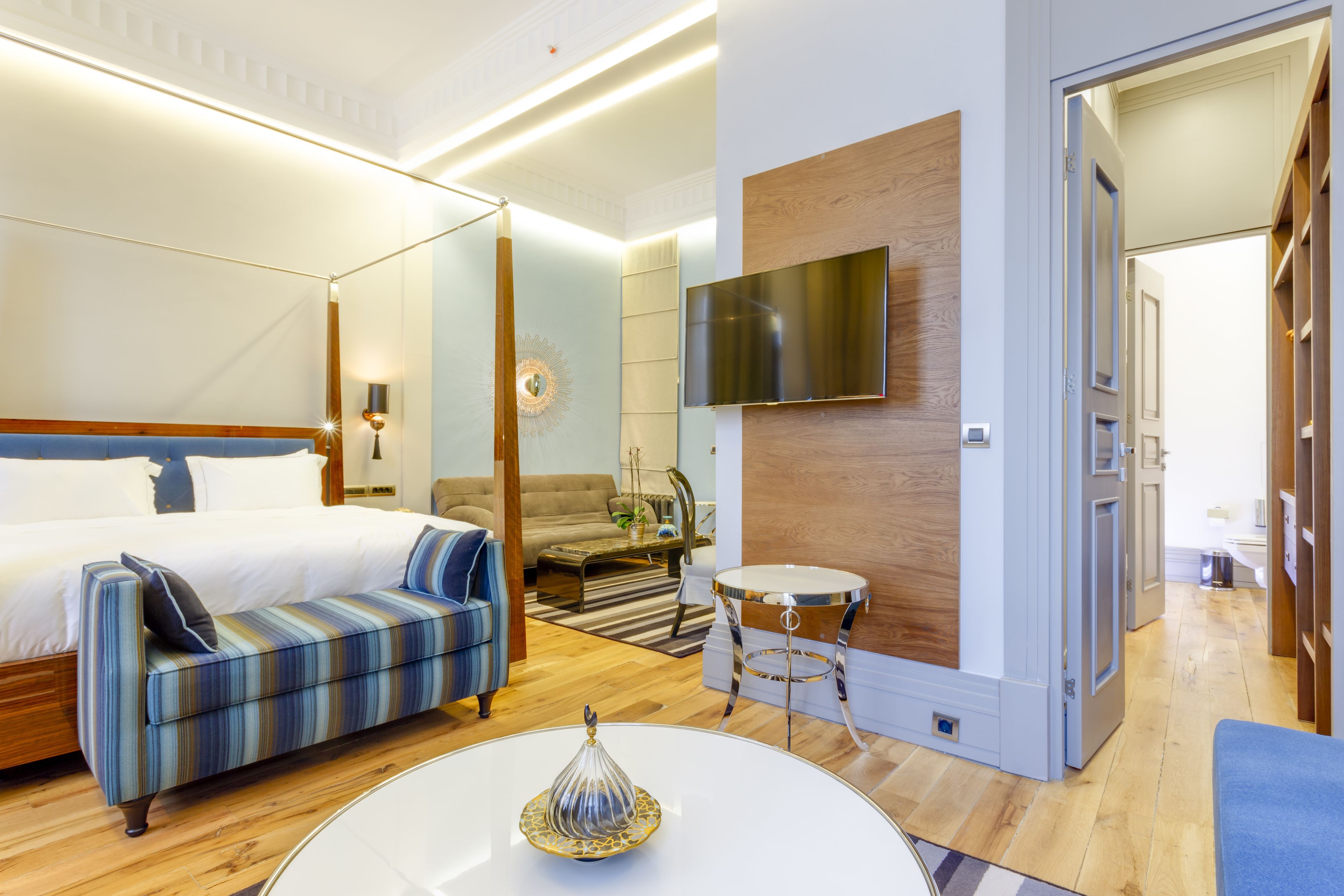 Une chambre d’hôtel moderne avec un grand lit, un canapé, un téléviseur fixé au mur et une petite table ronde.