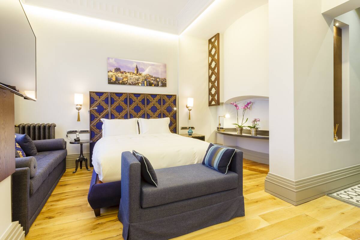 A hotel room with a large bed, a sofa, a small table, and a decorative wall piece.
