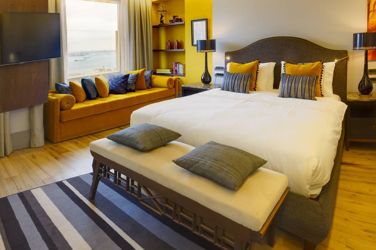 A hotel room with a large bed, a sofa, a bench, a TV, and a view of the sea.