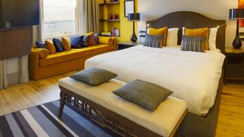 Une chambre d’hôtel avec un grand lit, un canapé, une banquette, une télévision et une vue sur la mer.