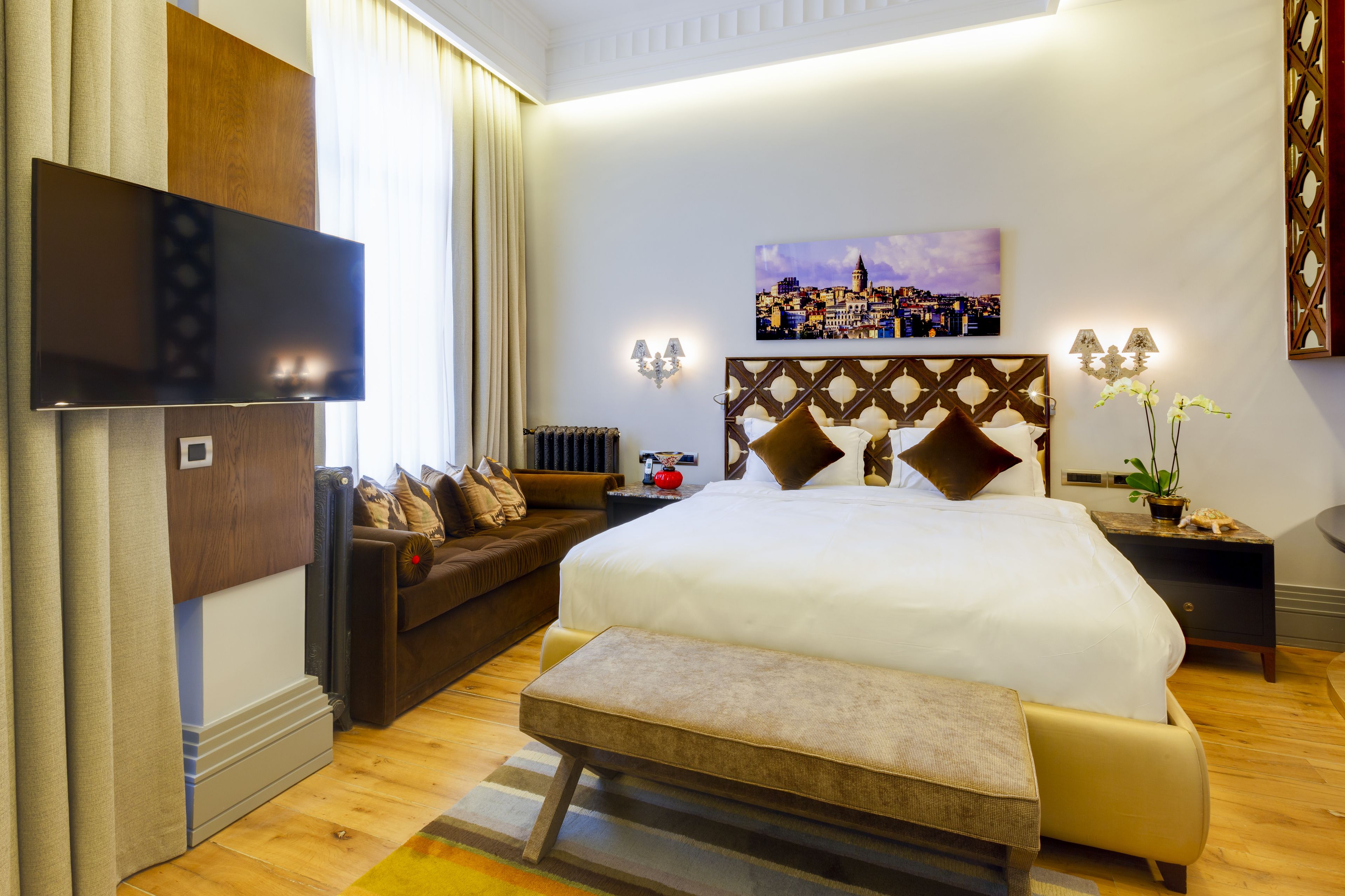 Une chambre d’hôtel avec un grand lit, un canapé, une télévision et un tableau représentant un paysage urbain.