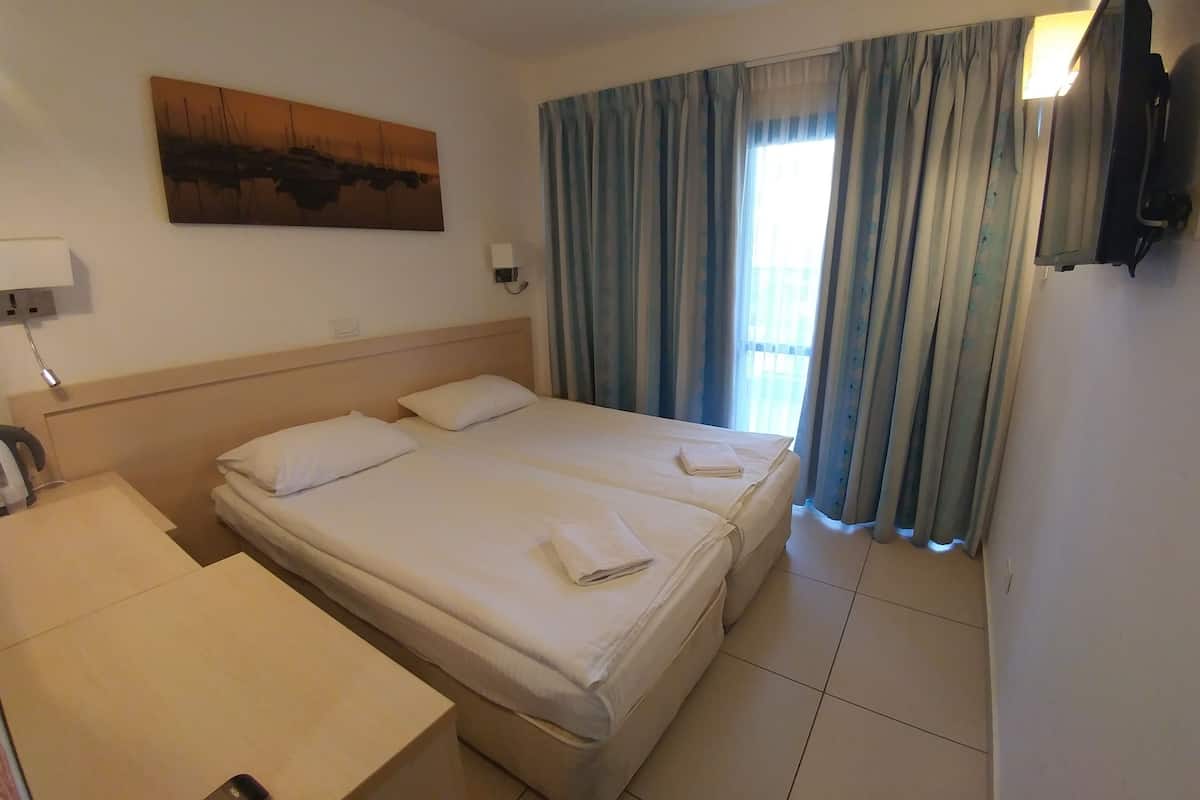A hotel room with a bed, a desk, a chair, a TV, and a painting on the wall.