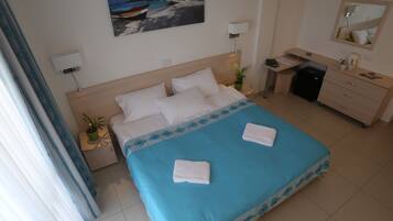Una camera d'albergo con un letto, una scrivania, una sedia, un comò, uno specchio, una pianta in vaso e un quadro appeso al muro.