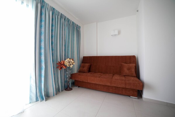 A living room with a brown sofa, a vase with flowers, and blue curtains with a floral pattern.