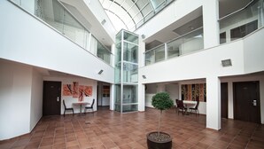 Un vaste atrium doté d’un haut plafond, de murs en verre et d’un arbre planté dans un grand pot au centre.