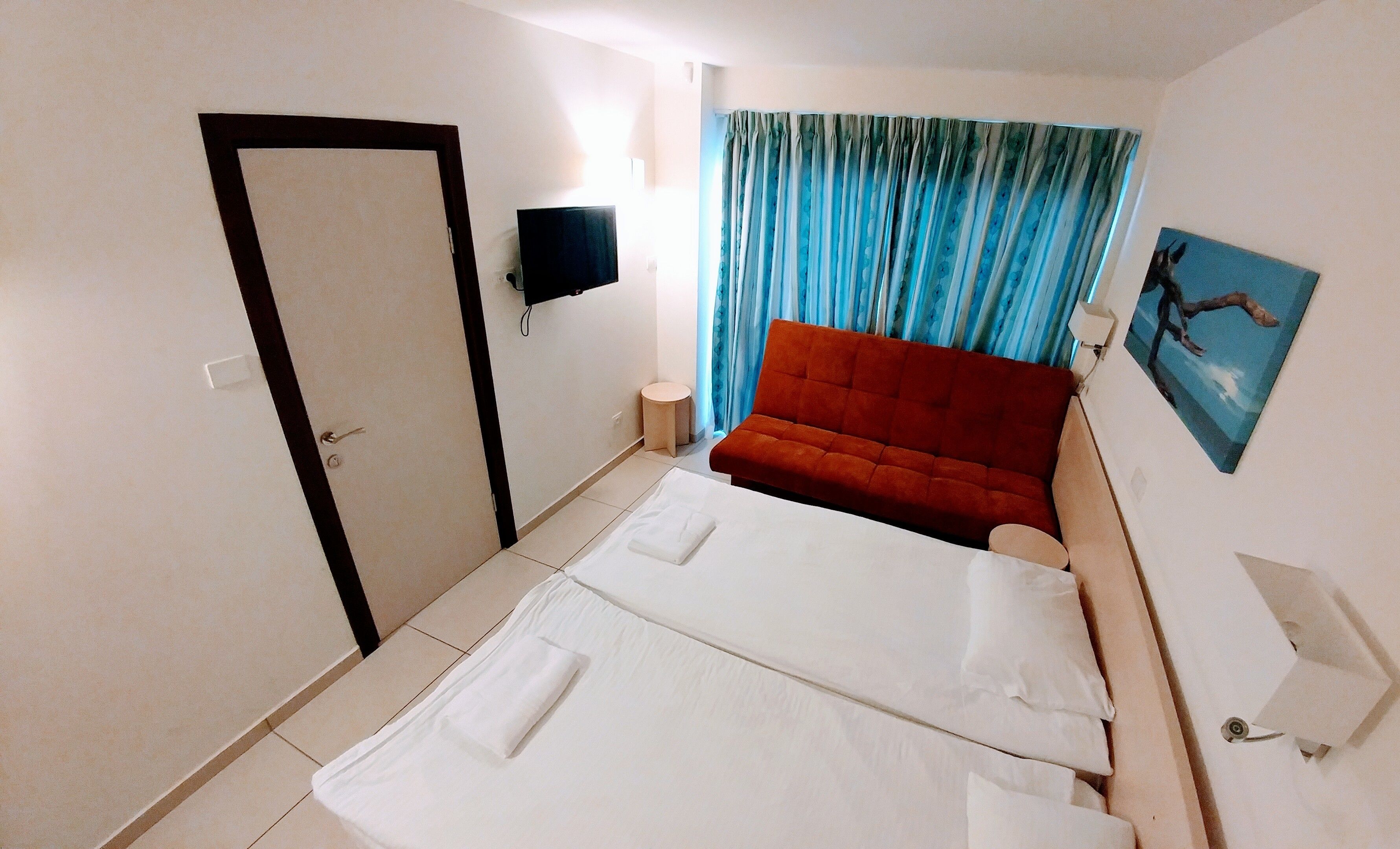 A hotel room with a bed, a red sofa, a TV, and a painting on the wall.