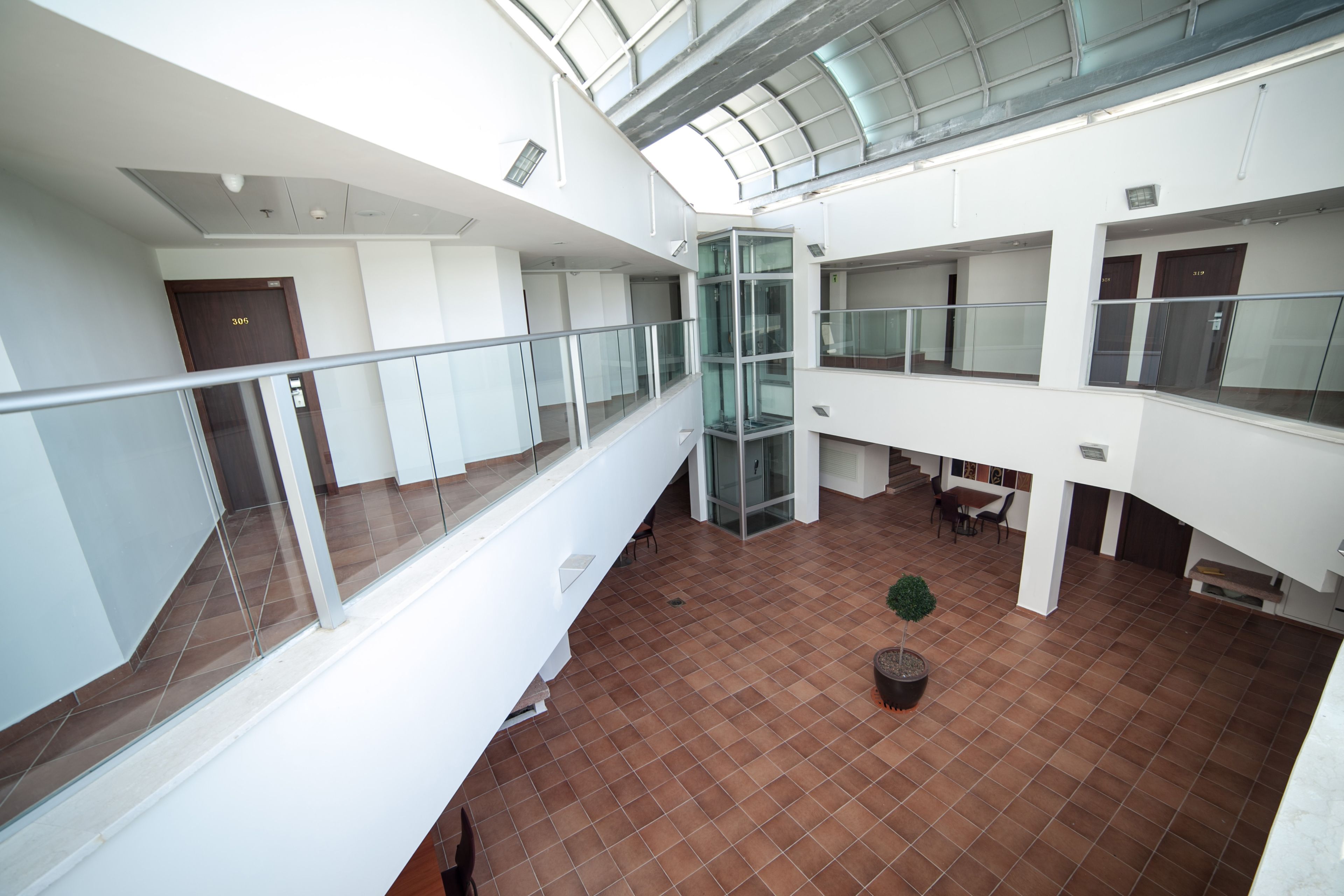 Ein mehrgeschossiges Interieur mit Glasgeländern, einem zentralen Aufzug und einem gefliesten Boden.