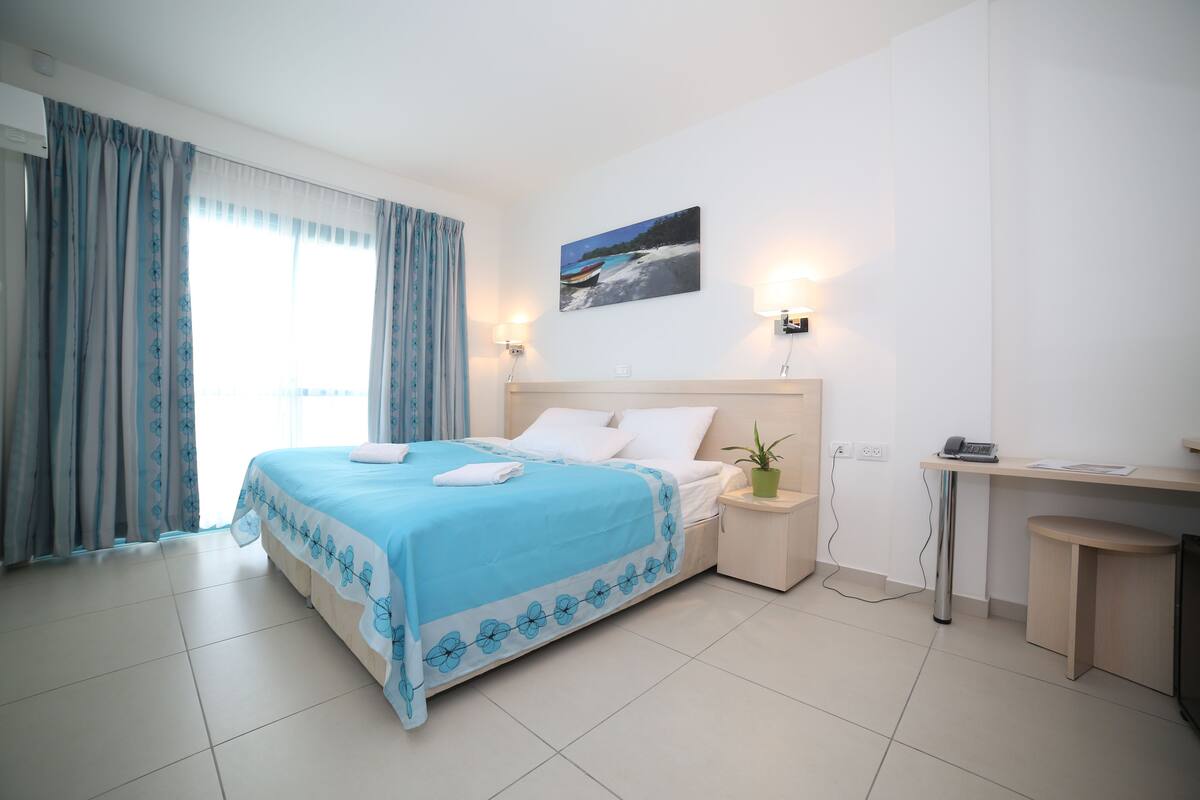 A neatly arranged hotel room with a bed, bedside table, and a desk.