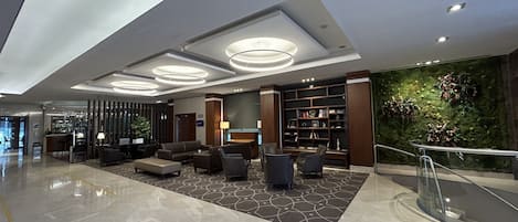 A modern lobby with a seating area, a reception desk, and a large bookshelf.