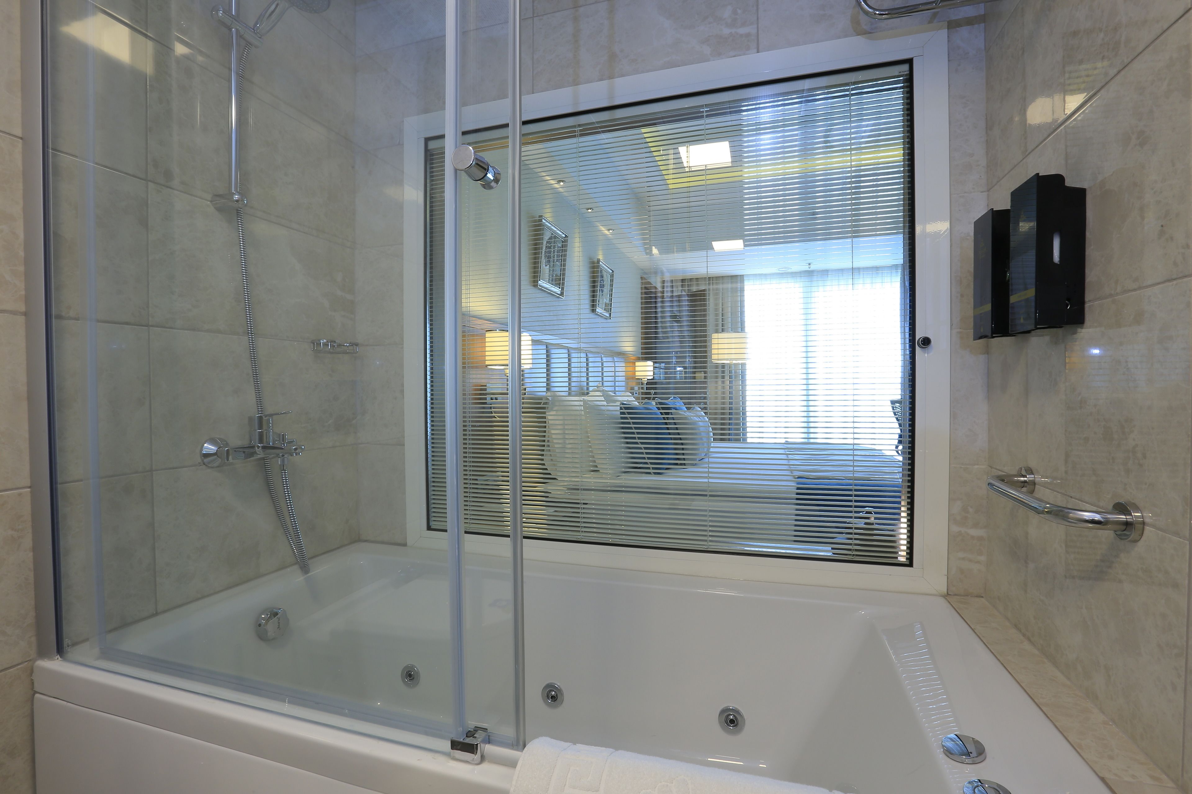 A modern bathroom with a glass-enclosed shower, a bathtub, and a window with blinds.