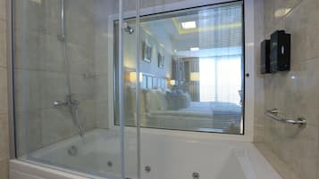 A modern bathroom with a glass-enclosed shower, a bathtub, and a window with blinds.