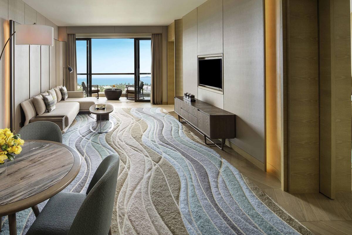 Ein modernes Hotelzimmer mit einer großen Couch, einem Esstisch, einem Flachbildfernseher und Blick auf den Ozean.