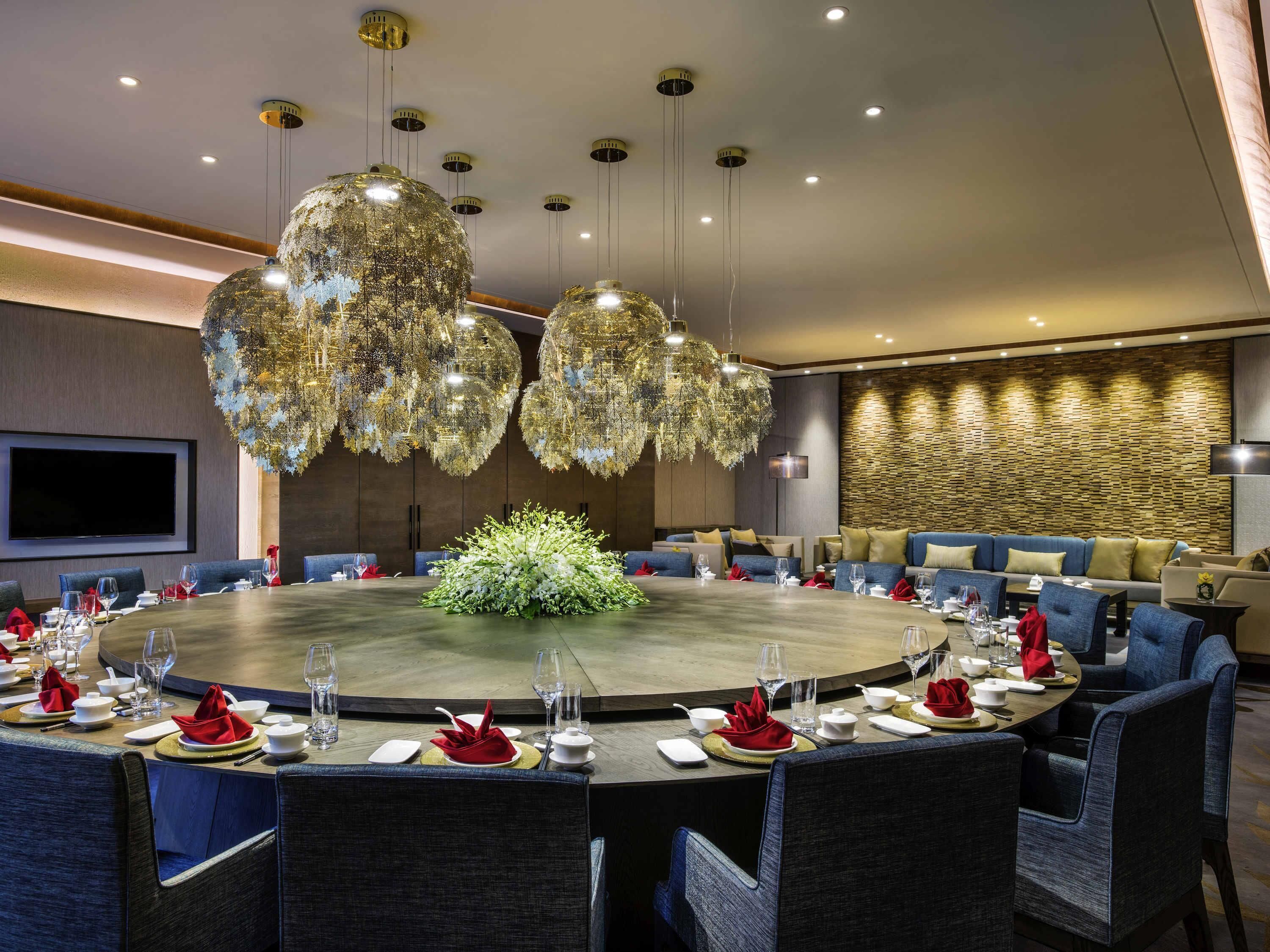 A round dining table with chairs, a central floral arrangement, and overhead hanging lights.