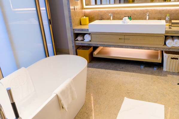 Un baño moderno con una bañera independiente, un espejo grande y un mueble de tocador con lavabo y espacio para toallas.