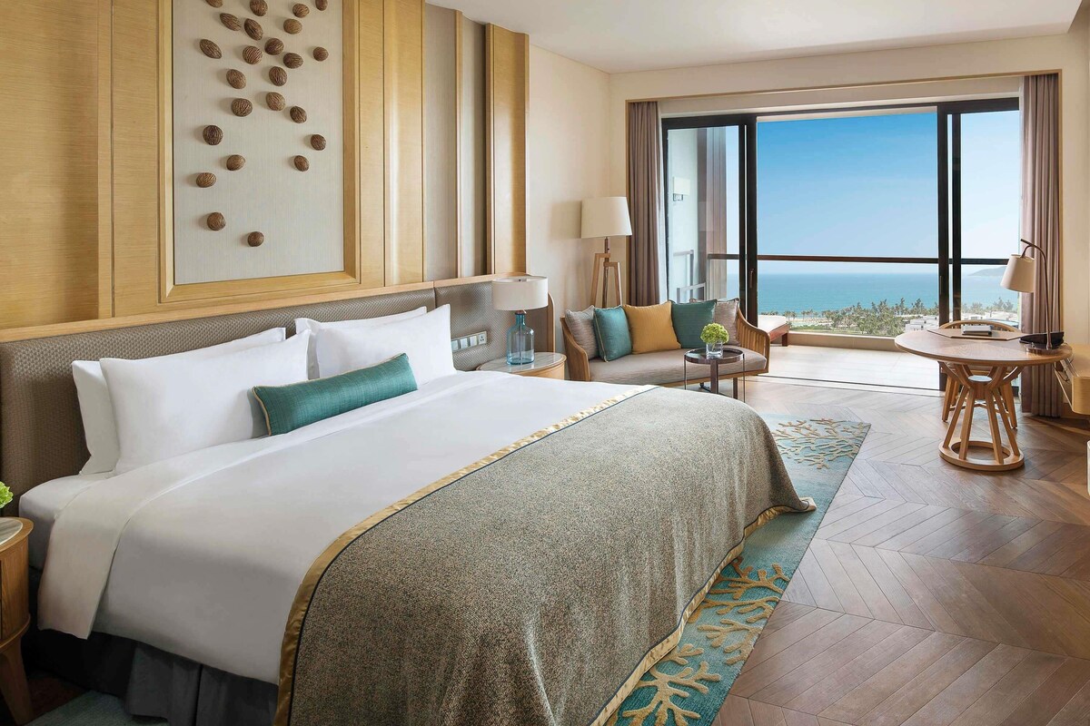 A hotel room with a large bed, a seating area with a table, and a view of the ocean.