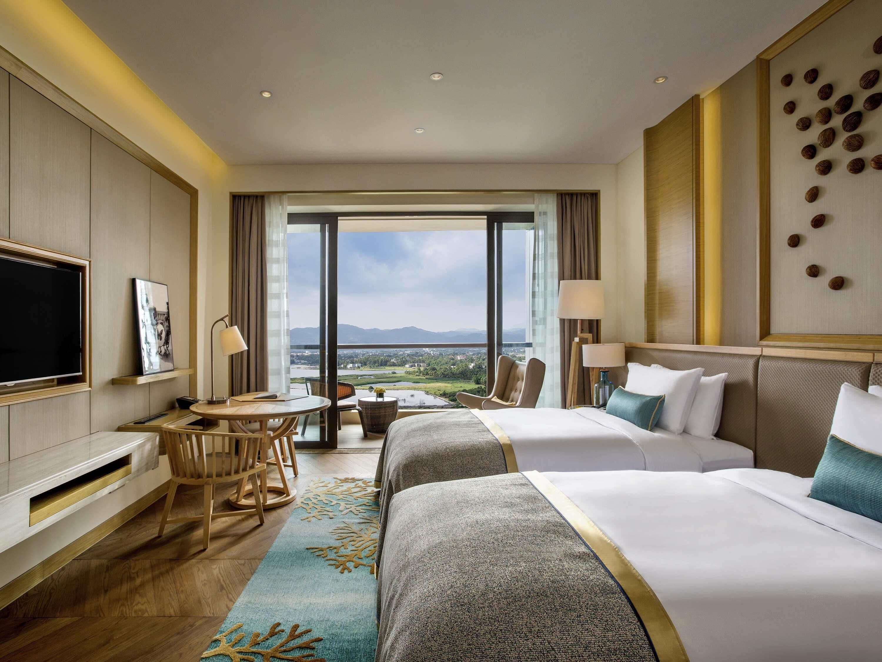A hotel room with a bed, a desk, a TV, and a view of the landscape.