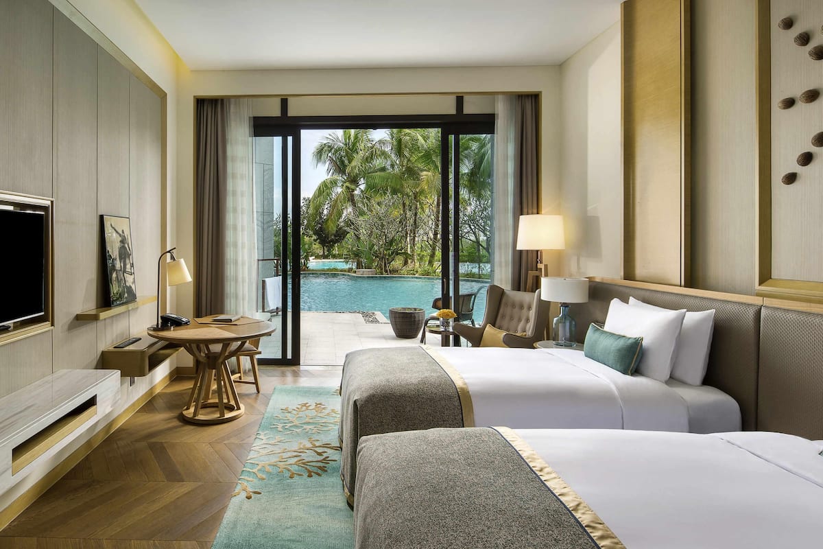 Une chambre d’hôtel avec deux lits, une télévision, un bureau avec une chaise, une lampe et une vue sur une piscine.