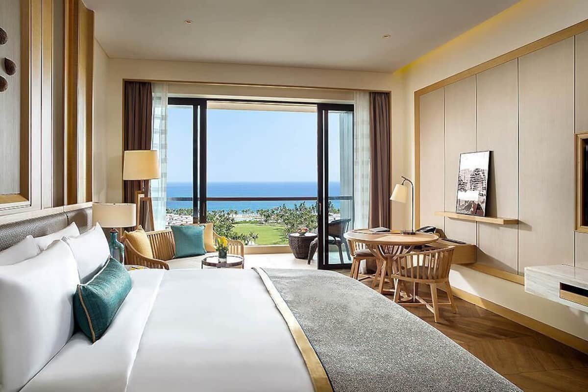 Ein Hotelzimmer mit einem großen Bett, einem Schreibtisch und Blick aufs Meer.