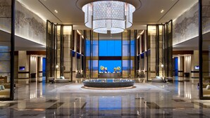 Um hall amplo com uma fonte central, tetos altos e um grande lustre.