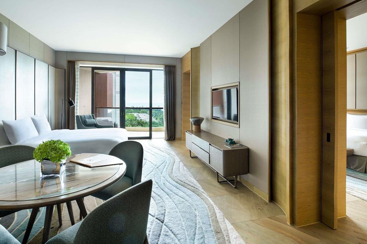 Une chambre d’hôtel moderne équipée d’un lit, d’un coin repas, d’une télévision et d’un balcon avec vue.