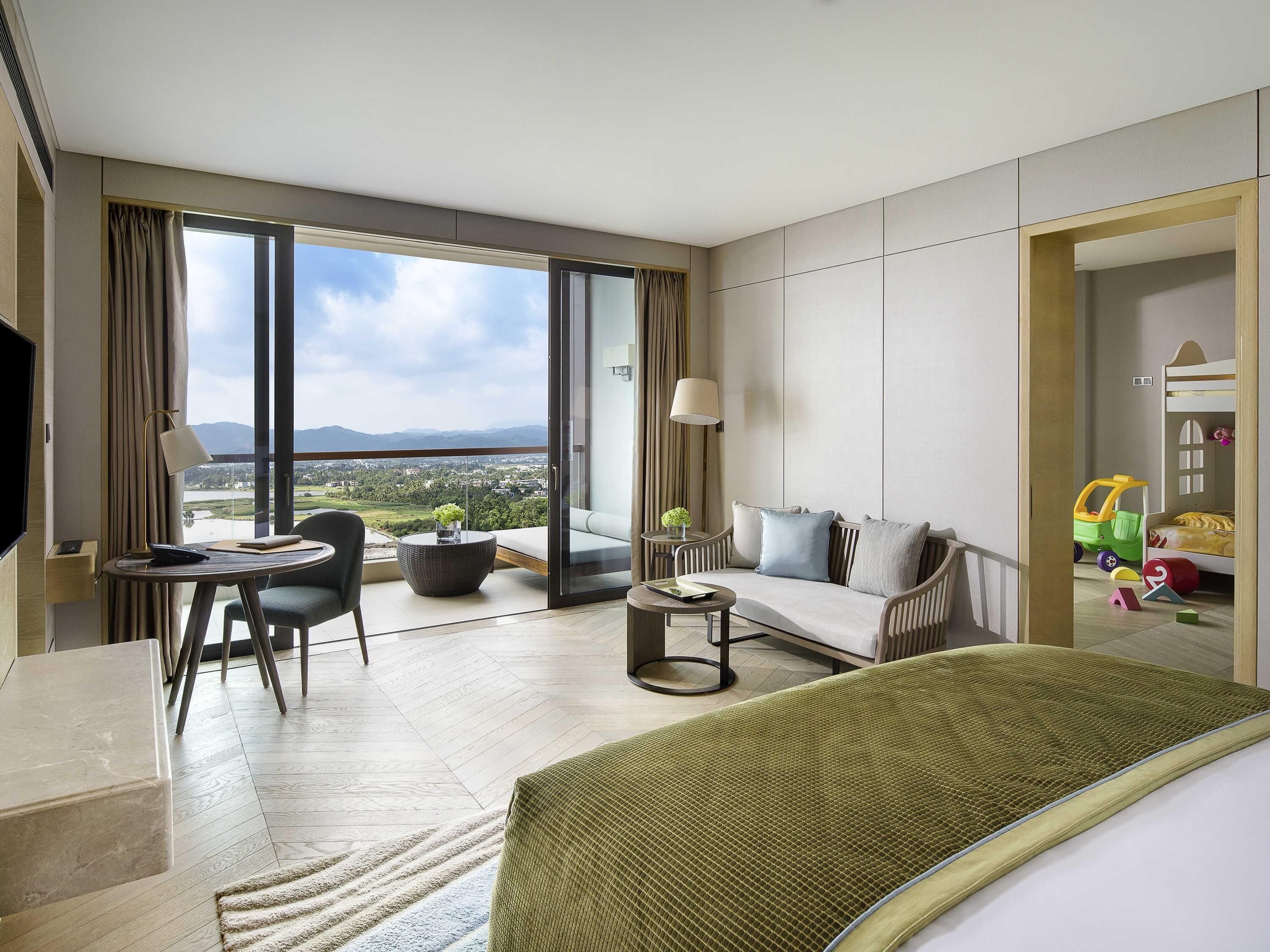 Een hotelkamer met balkon, een zithoek, een eethoek en een kinderspeelruimte.