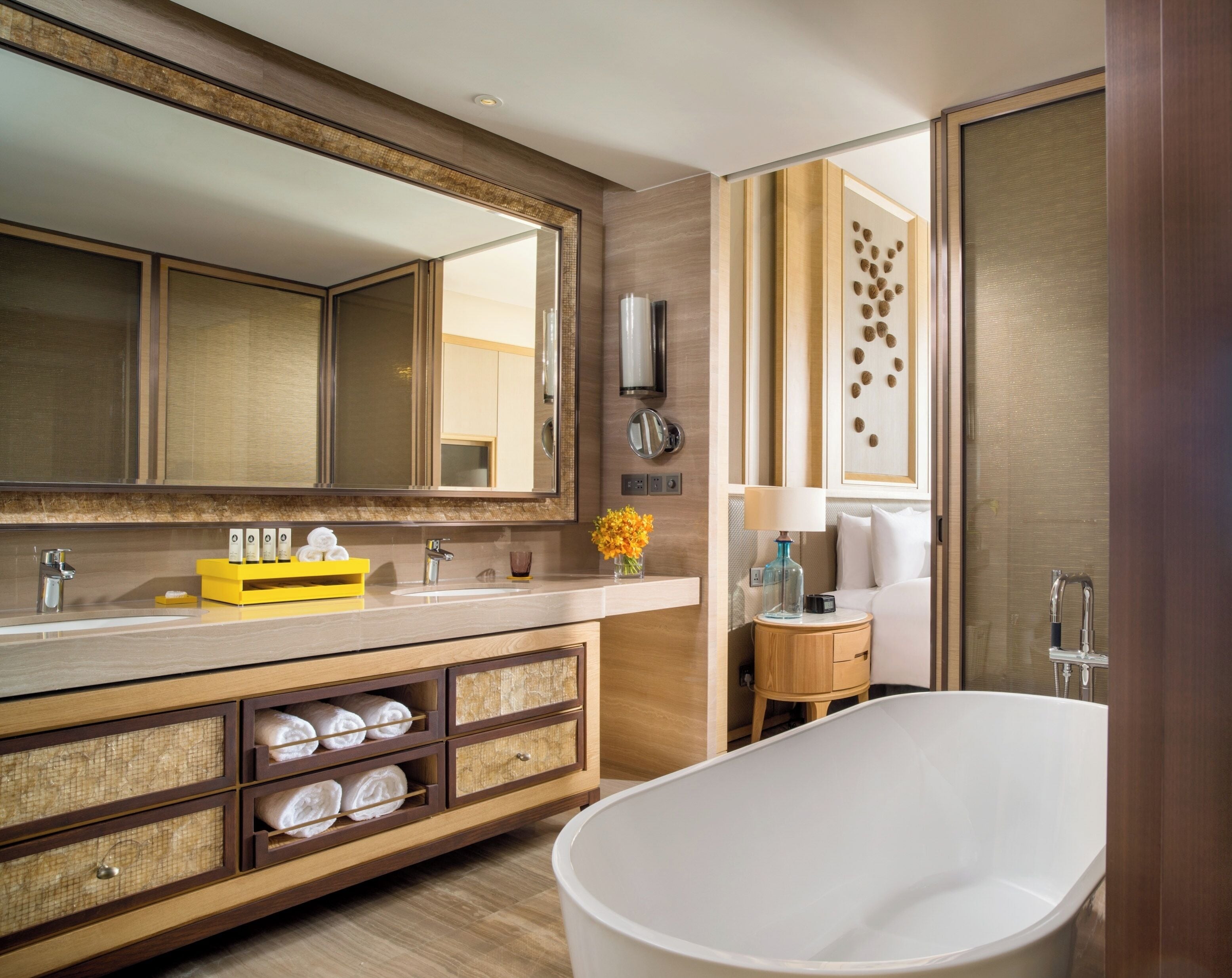 A modern bathroom with a large mirror, a freestanding bathtub, a vanity with a yellow soap dish, and a decorative wall piece.