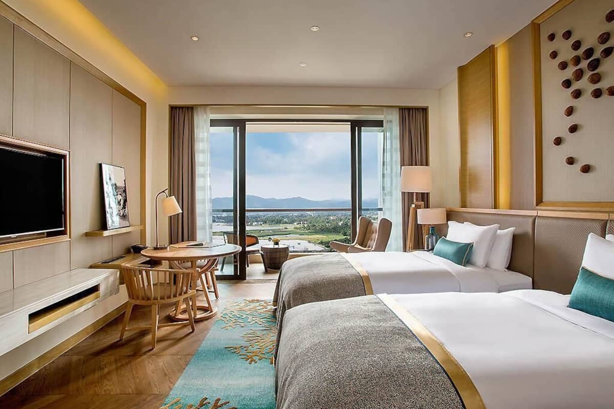 Une chambre d’hôtel avec deux lits, une télévision, un bureau avec une chaise, une vue sur l’extérieur et une grande fenêtre.