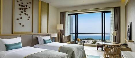 A hotel room with two beds, a desk, a chair, a large window with a view, and a decorative wall piece.