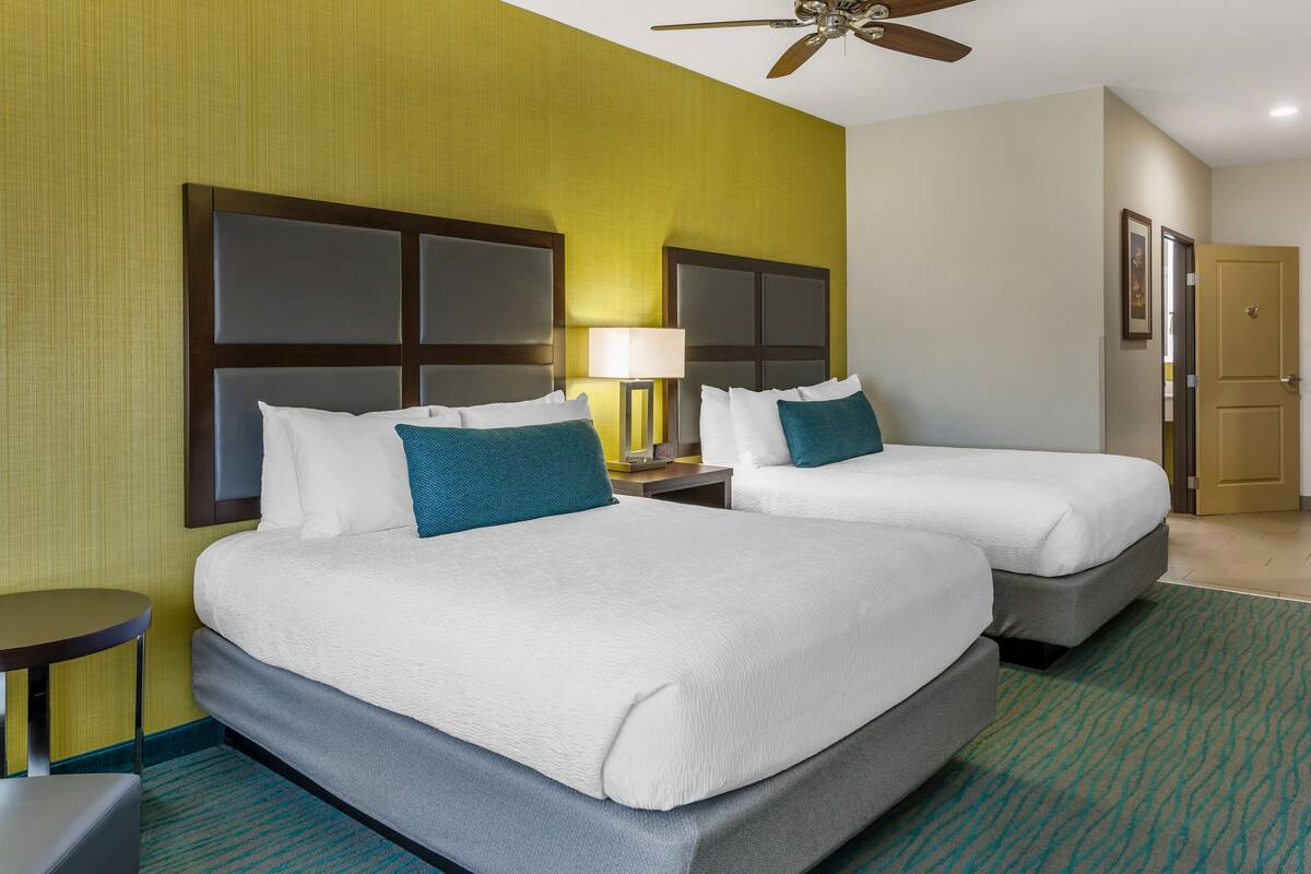 A hotel room with two beds, a nightstand, a lamp, and a ceiling fan.