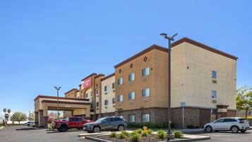 Ein Hotel mit zentralem Eingang, mehreren Stockwerken und einem Parkplatz mit einigen Autos.