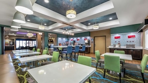 A hotel lobby with multiple seating areas, a bar, and a kitchen visible in the background.