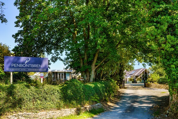 A sign for Penbontbren Bed & Breakfast Suites with a stone wall and greenery.