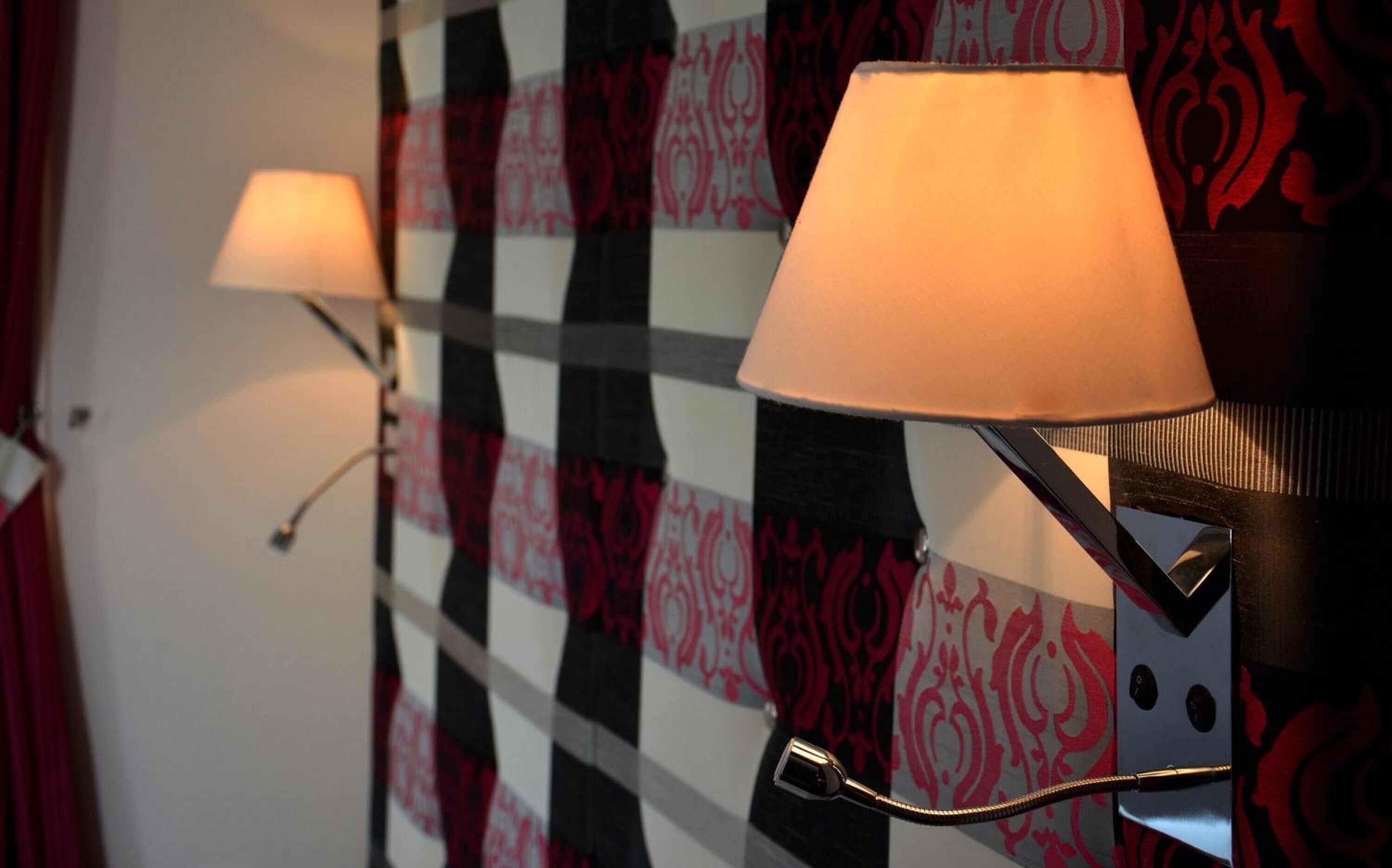 Two wall-mounted lamps with adjustable arms in a room with patterned wallpaper.