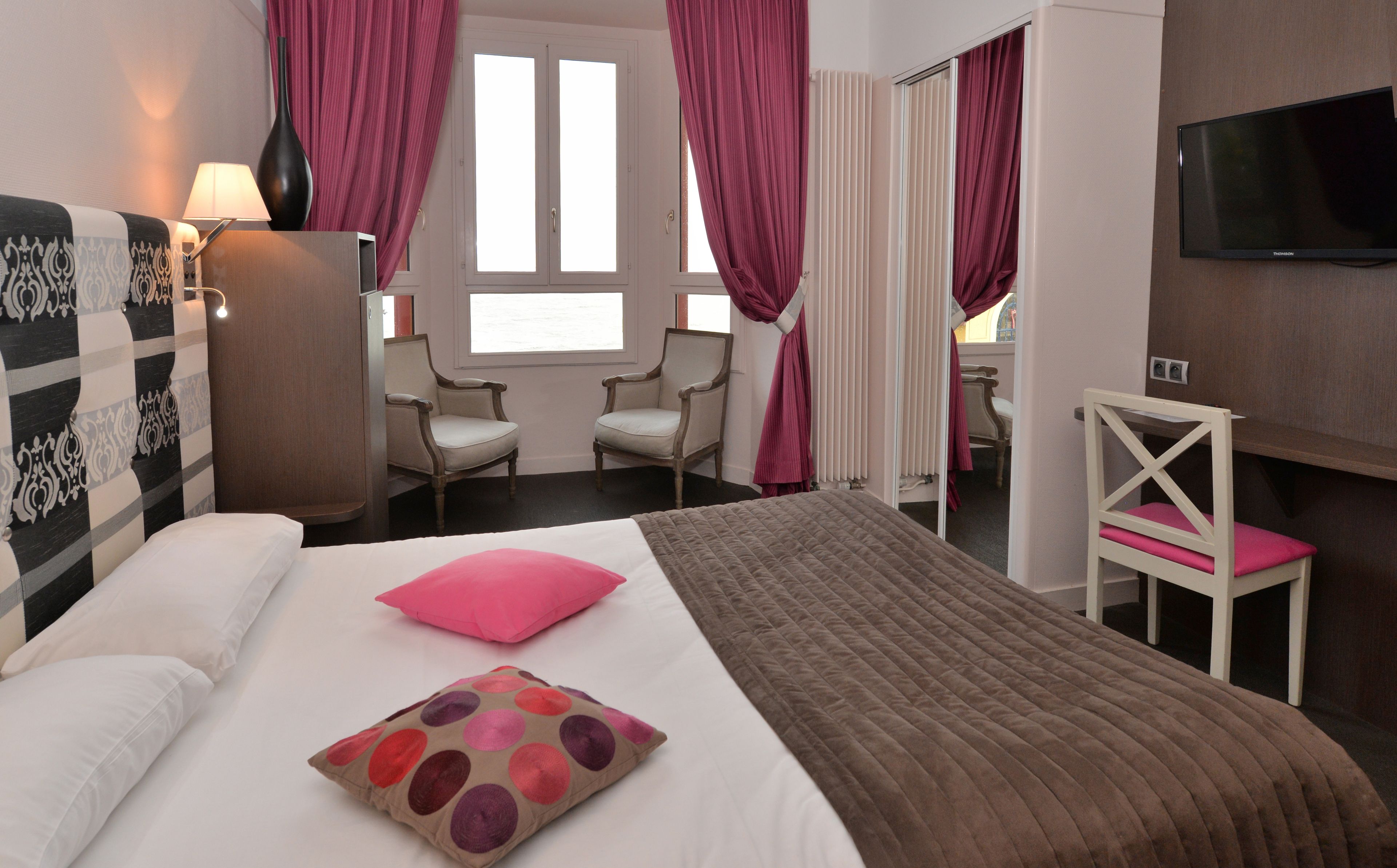 A hotel room with a bed, a chair, a desk, a TV, and a window with curtains.